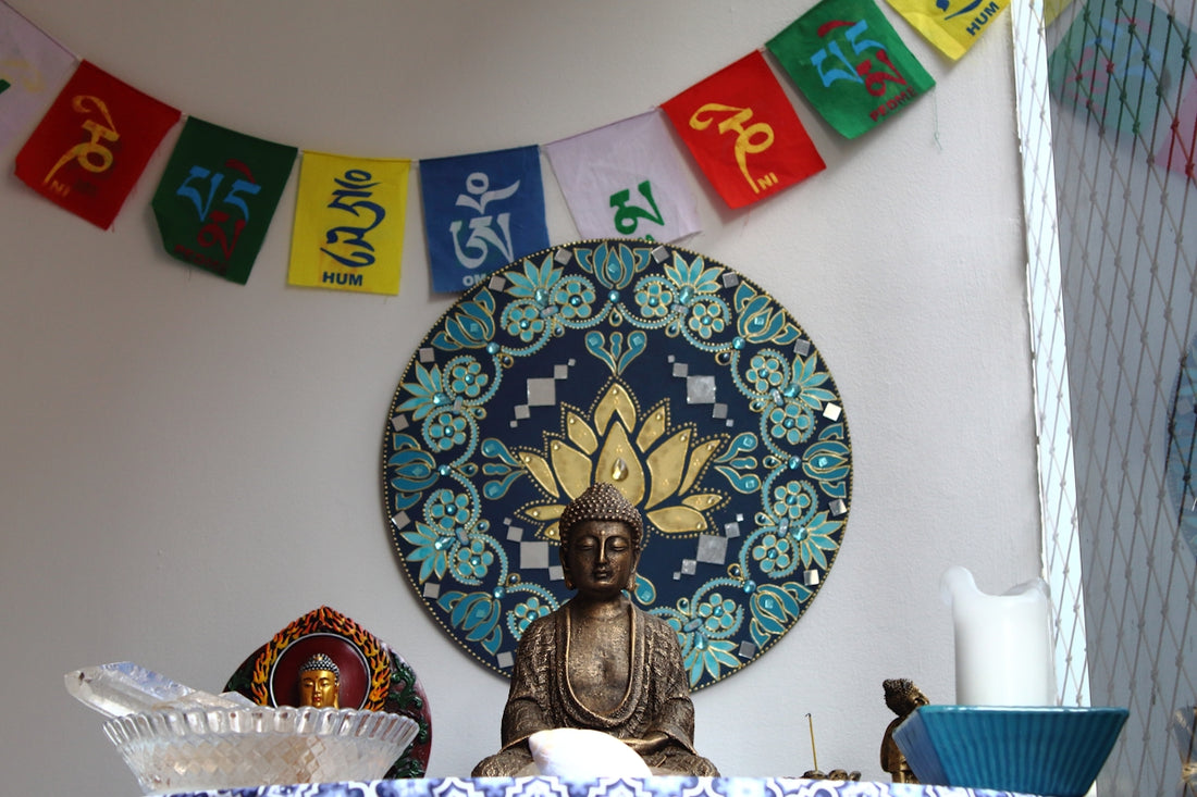 Buddha statue with prayer flags and lotus mandala.
