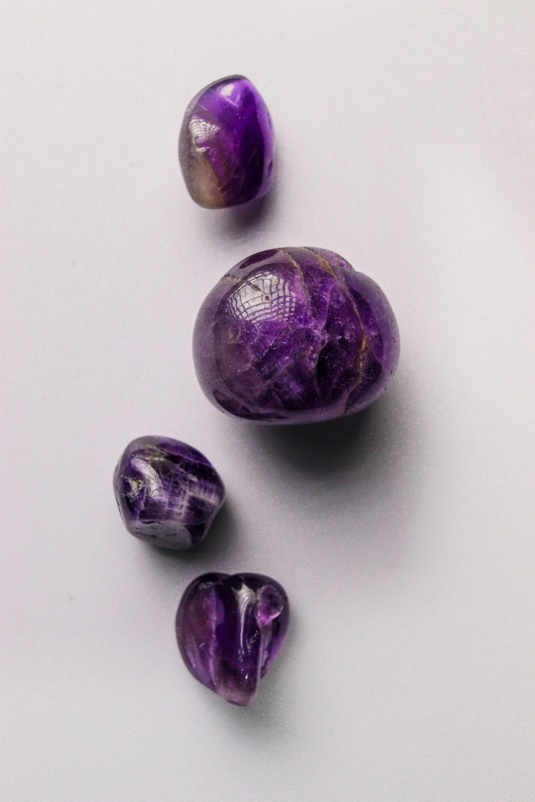 Four polished purple amethyst stones on a light background.