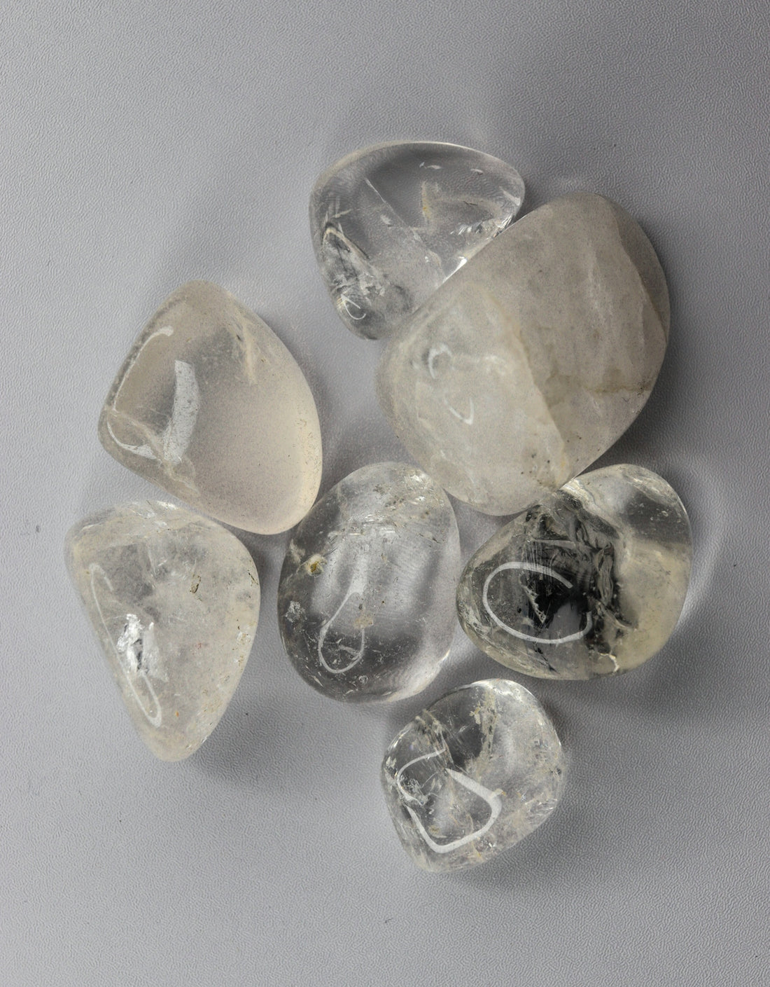 Several clear tumbled quartz stones on a light background.