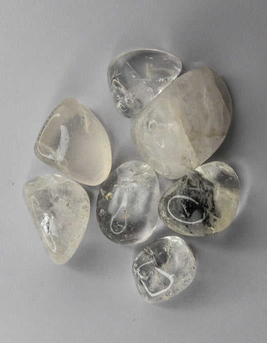 Several clear tumbled quartz stones on a light background.