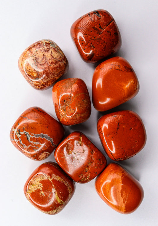 Tumbled red jasper stones scattered on a white surface.
